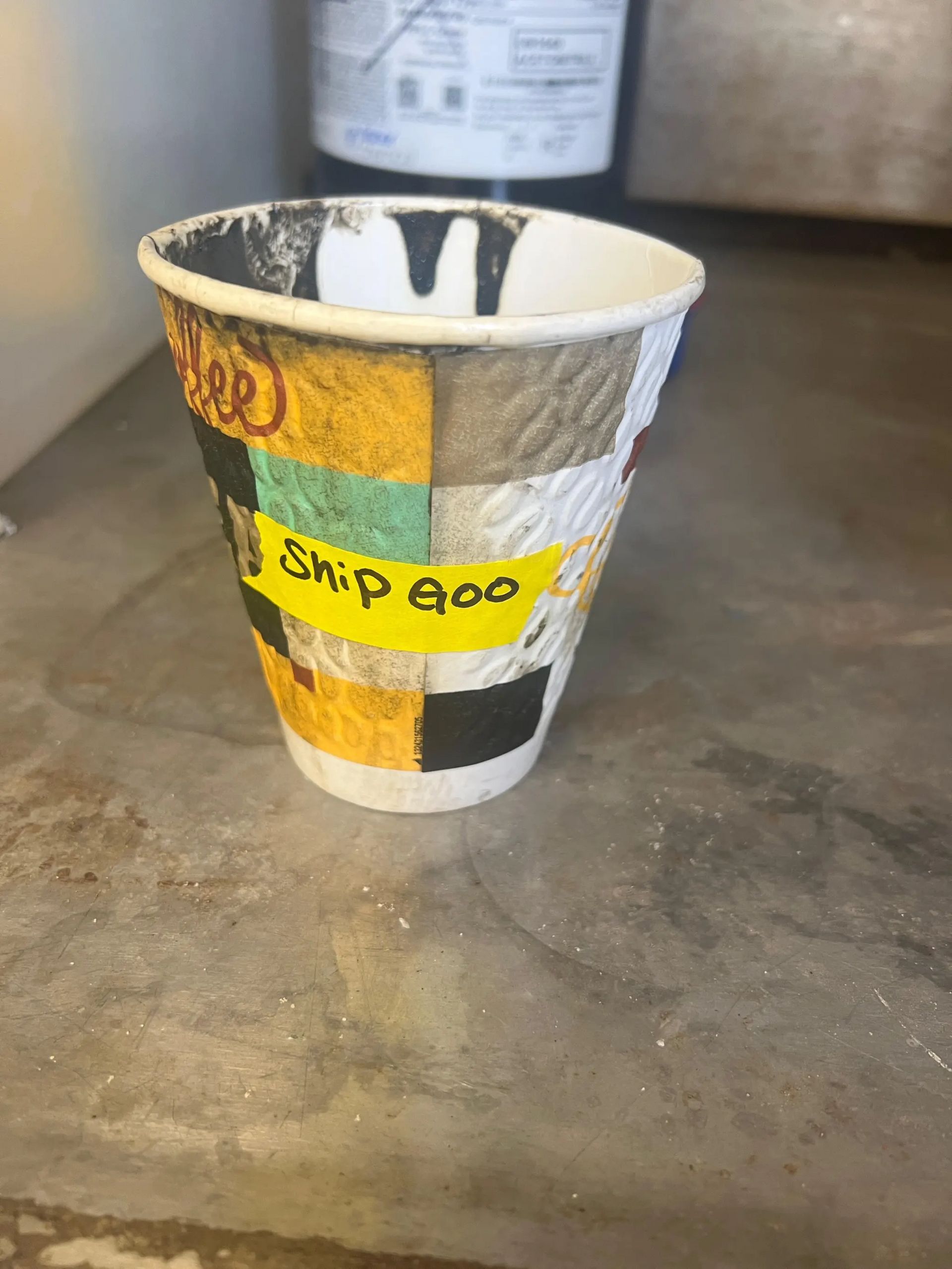 A battered paper cup with black goo around the edges, labeled with a pioece of yellow tape with “Ship Goo” written on it in sharpie. Science!
