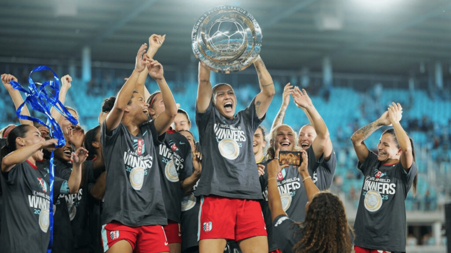 Kansas City forward Bia Zaneratto lifts the 2025 NWSL Shield as her Current teammates cheer.