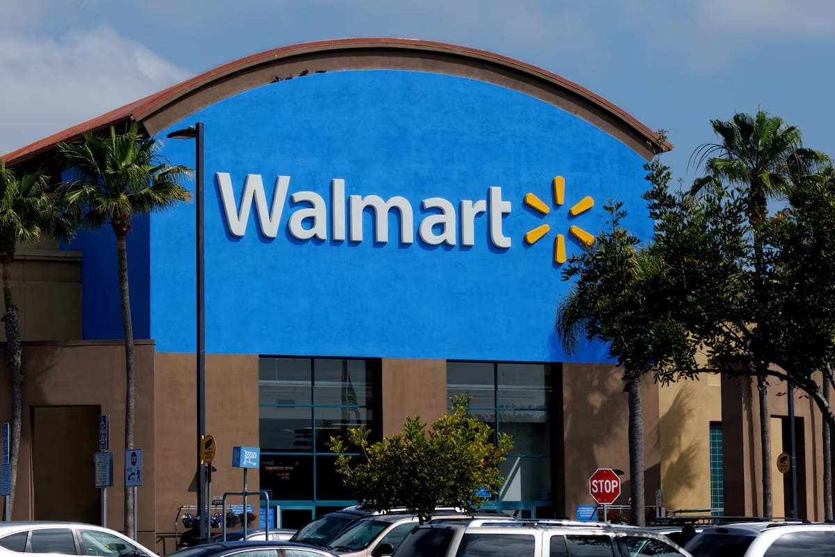 Façade d’un magasin Walmart bleu avec logo blanc et jaune, entourée de palmiers et de voitures sur le parking.