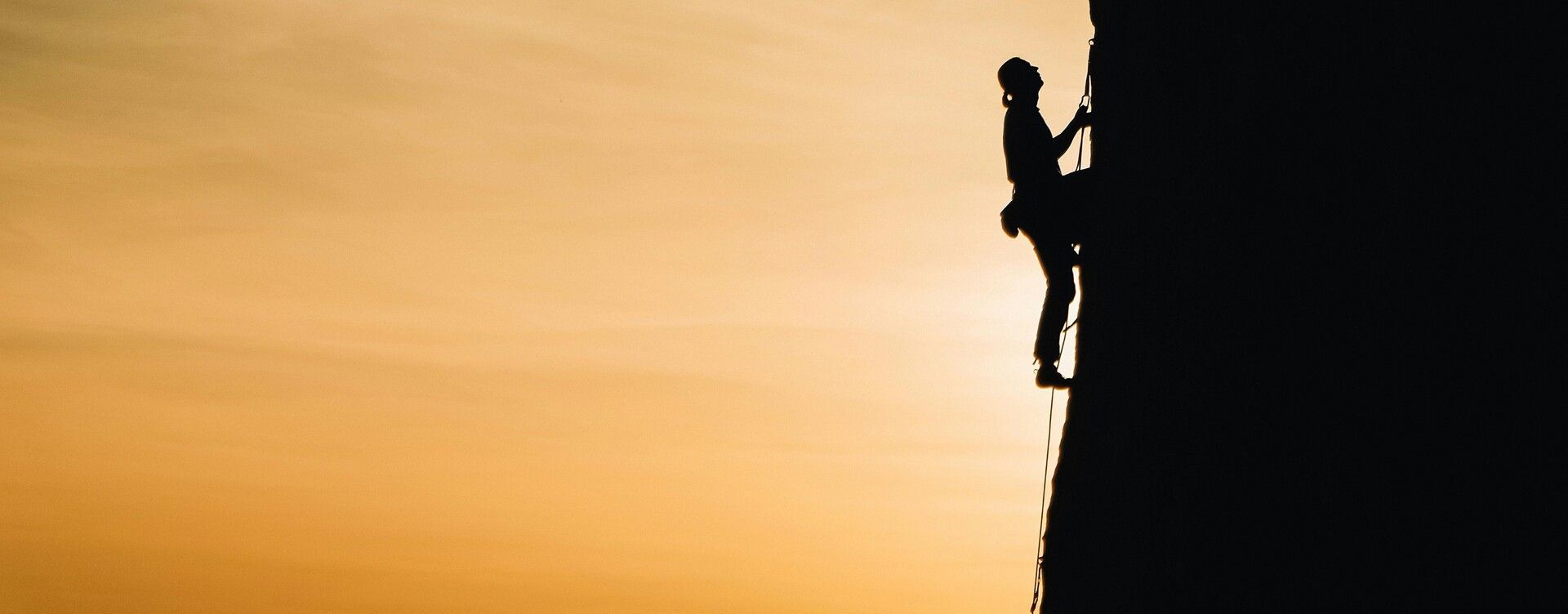 Silhouette of a person climbing a mountain at sunrise, representing growth and progress through challenges.