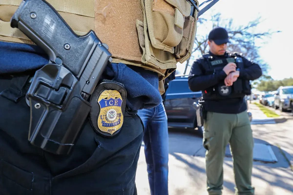 Close-up picture of an immigration officer's badge and gun, hanging from their jeans. 