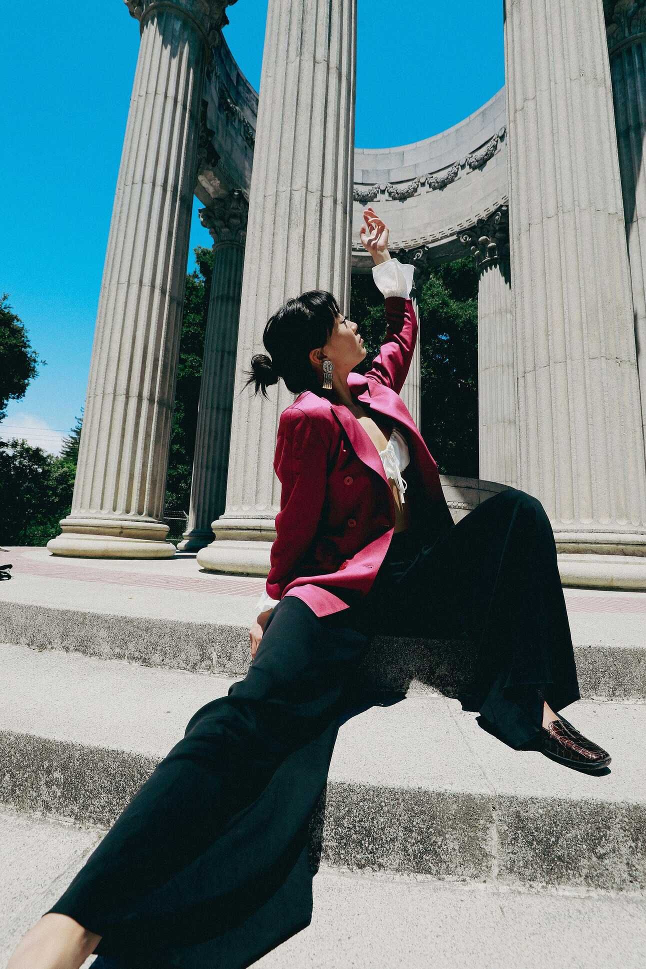 An asian woman wearing black pants and a pink blazer releasing her hand into the sky