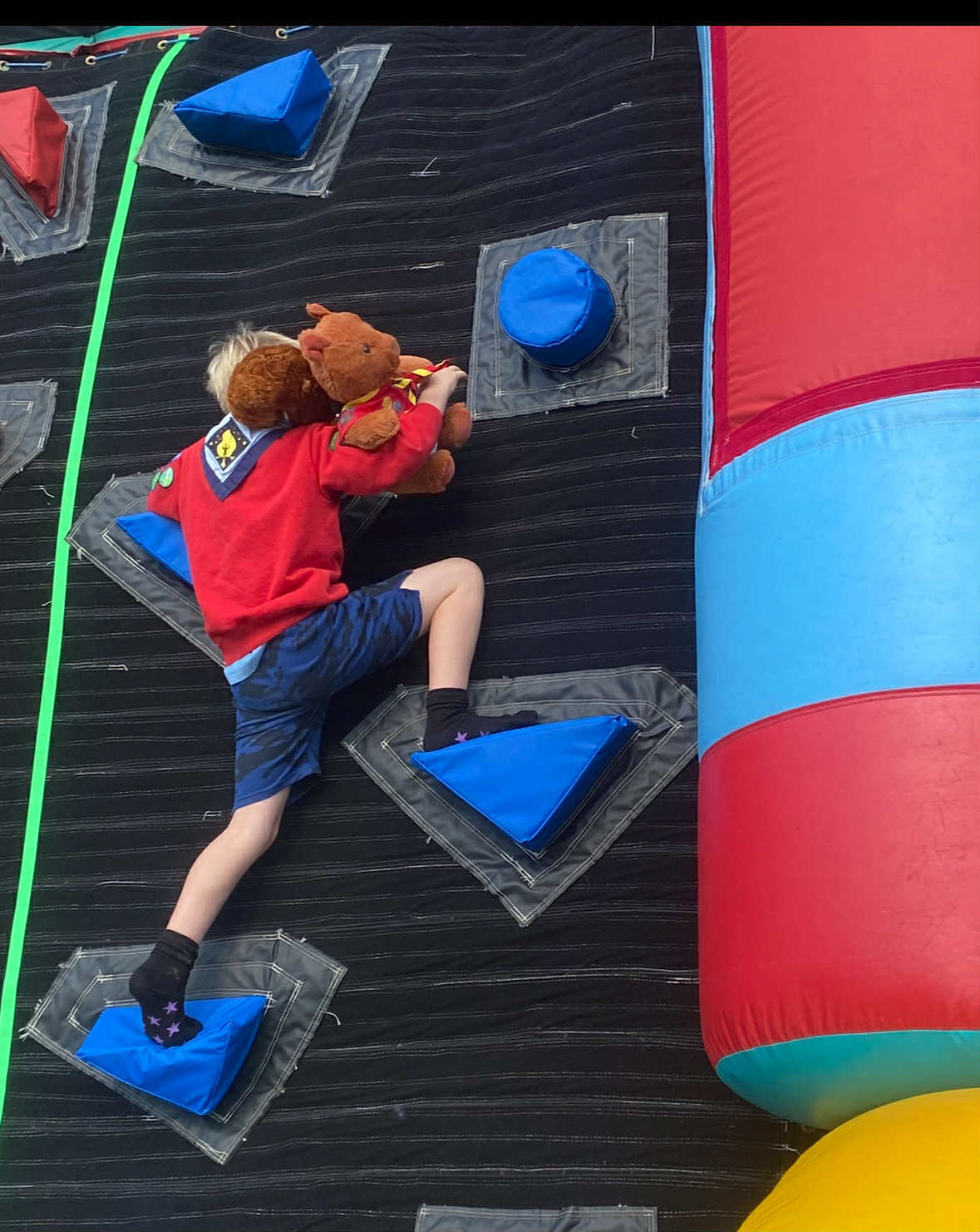a scout rock climbing on an indoor wall holding a teddy bear