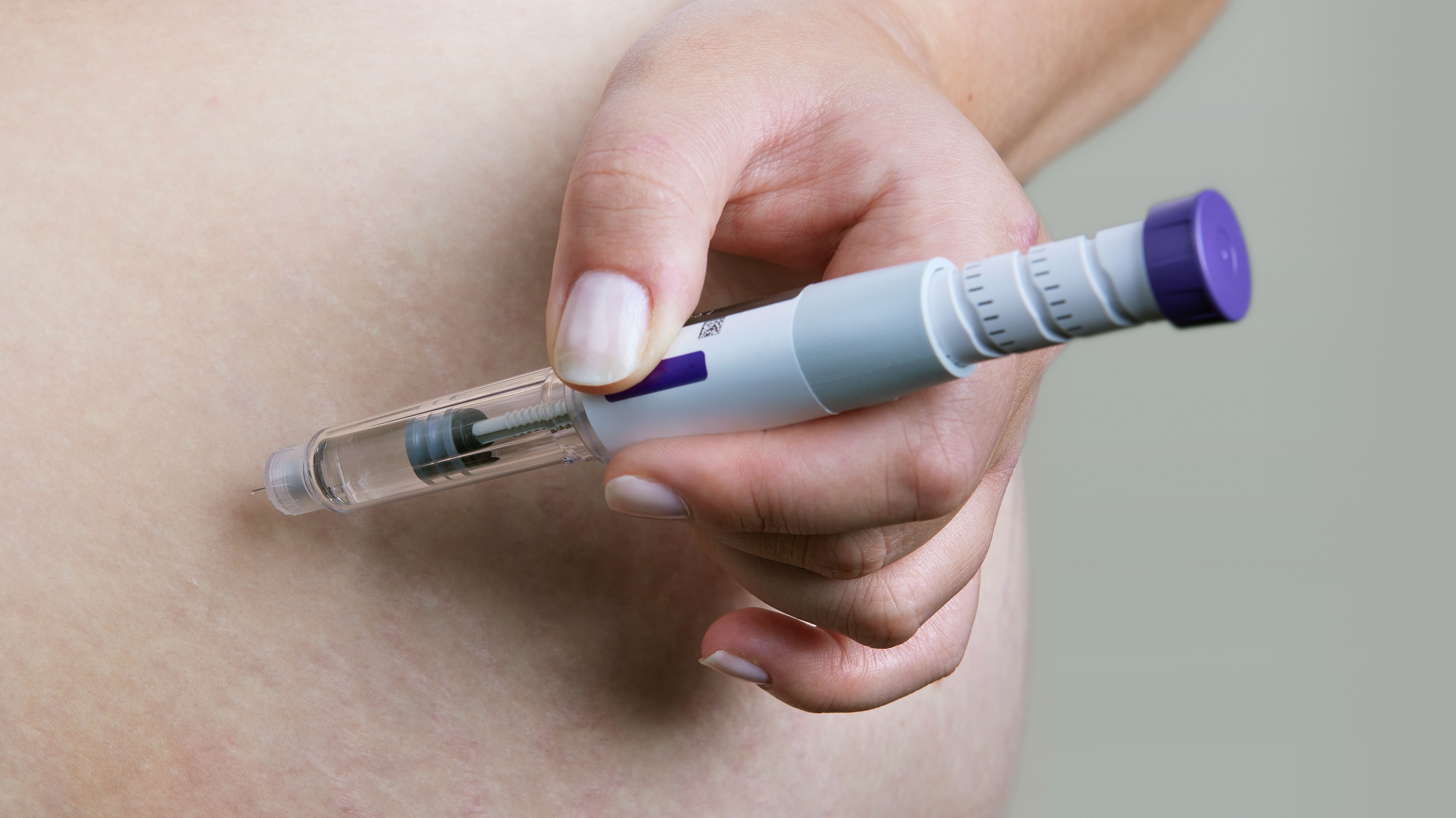 Person injecting a GLP-1 injection pen in their abdomen.