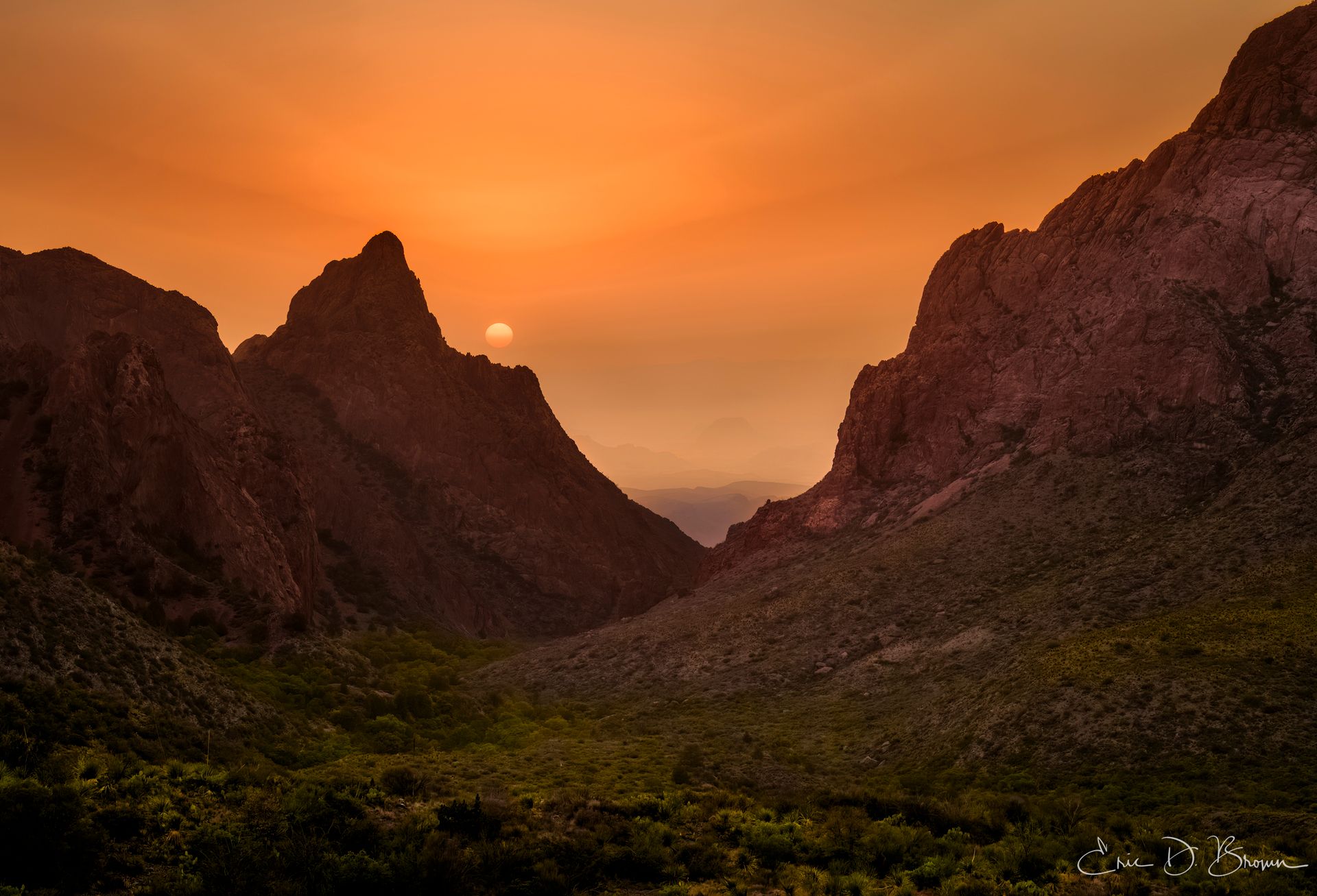 Golden sunset through a natural rock window formation at Big Bend National Park, with silhouetted mountains and desert landscape in warm orange and amber light