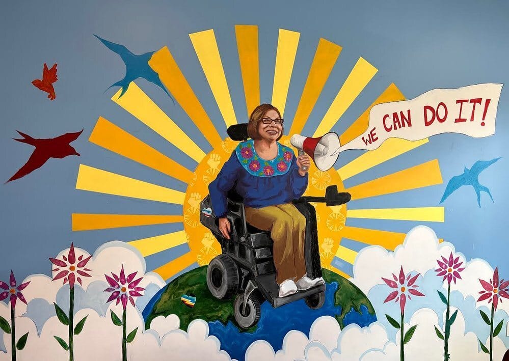 An illustration of Judy Heumann, in a wheelchair, with a megaphone and the words "we can do it" emmanating from it, surrounded by nature including the sun and birds in the background