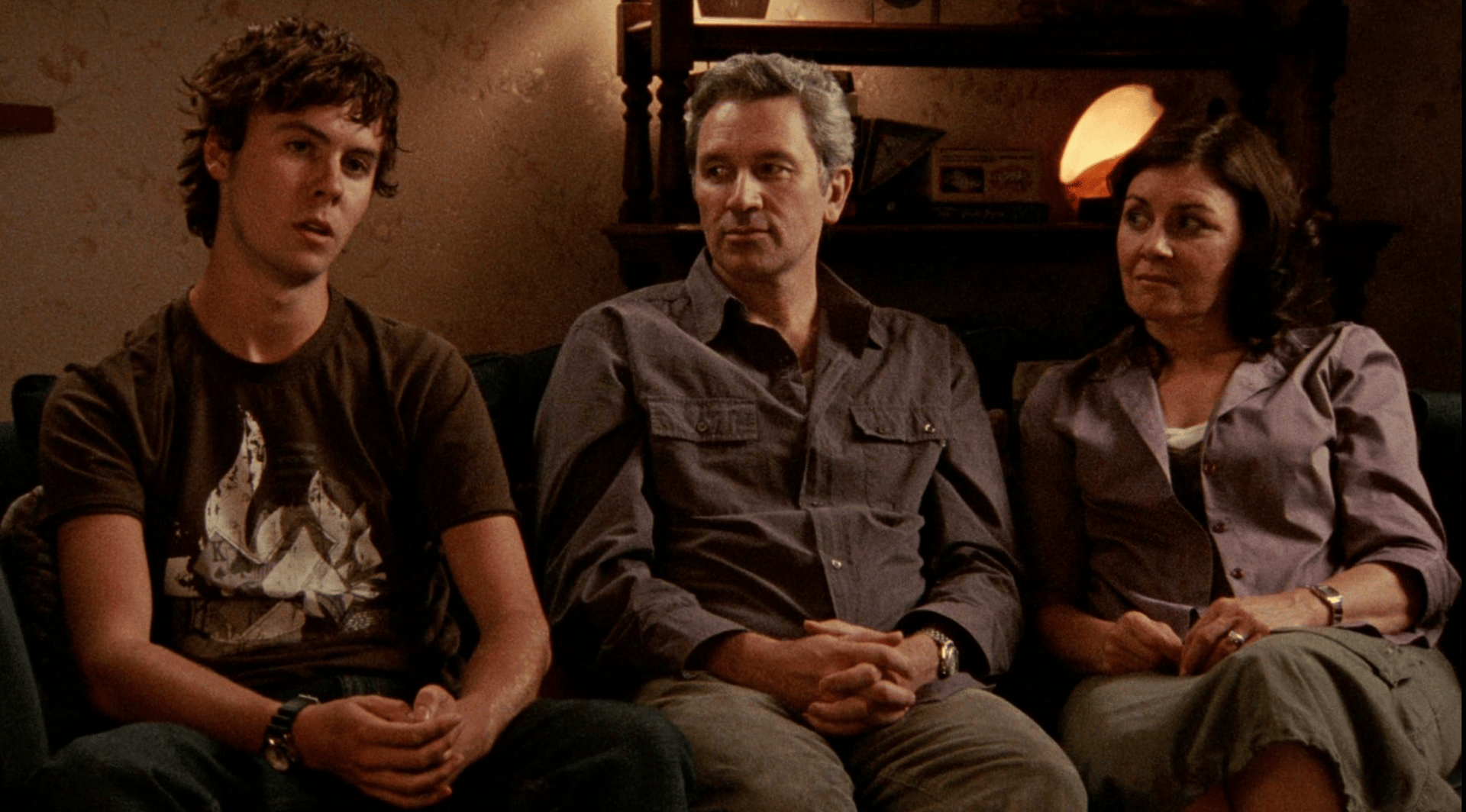 Screenshot from a faux-documentary, in which a family, husband, wife, and son sit talking to the camera.