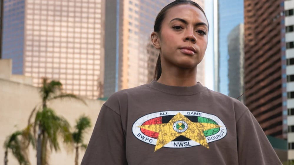 NWSL star Ally Brazier modeling the NWSL x BWPC Black History Month capsule t-shirt against an urban backdrop.