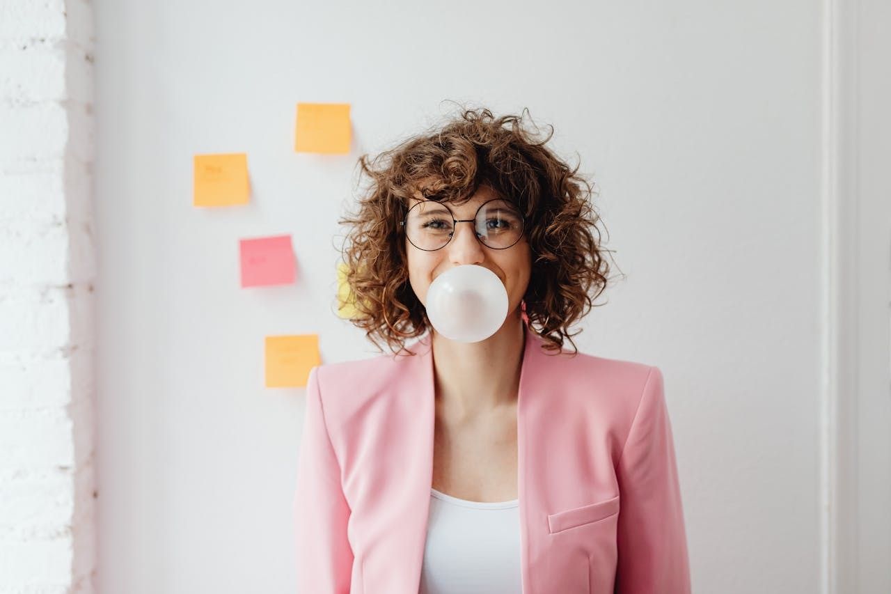 woman in pink blazer blowwing a bubble with gum