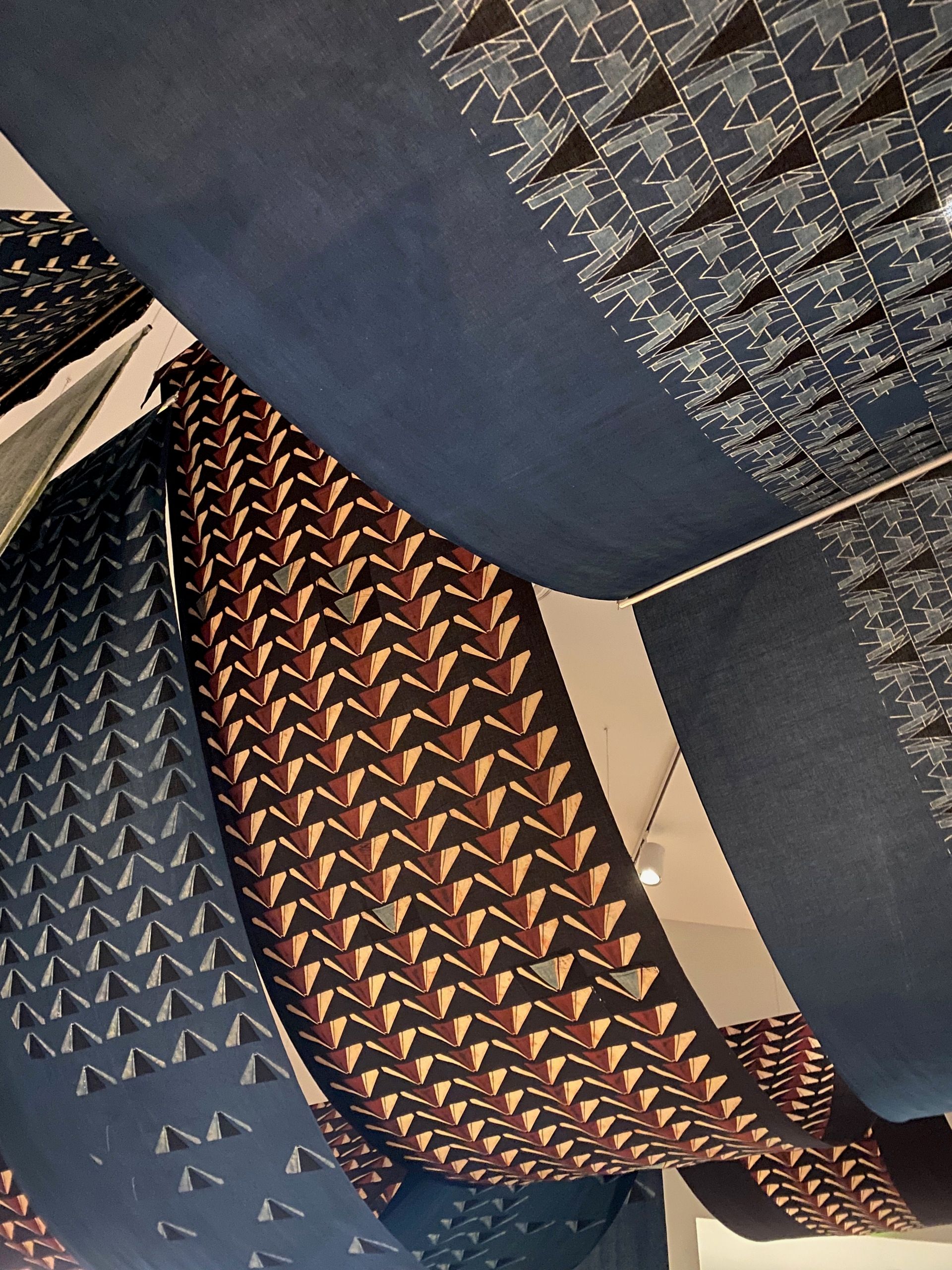 Close-up of block-printed textiles in shades of blue, brown, white, and gray, in various patterns, hanging down from and across the ceiling.