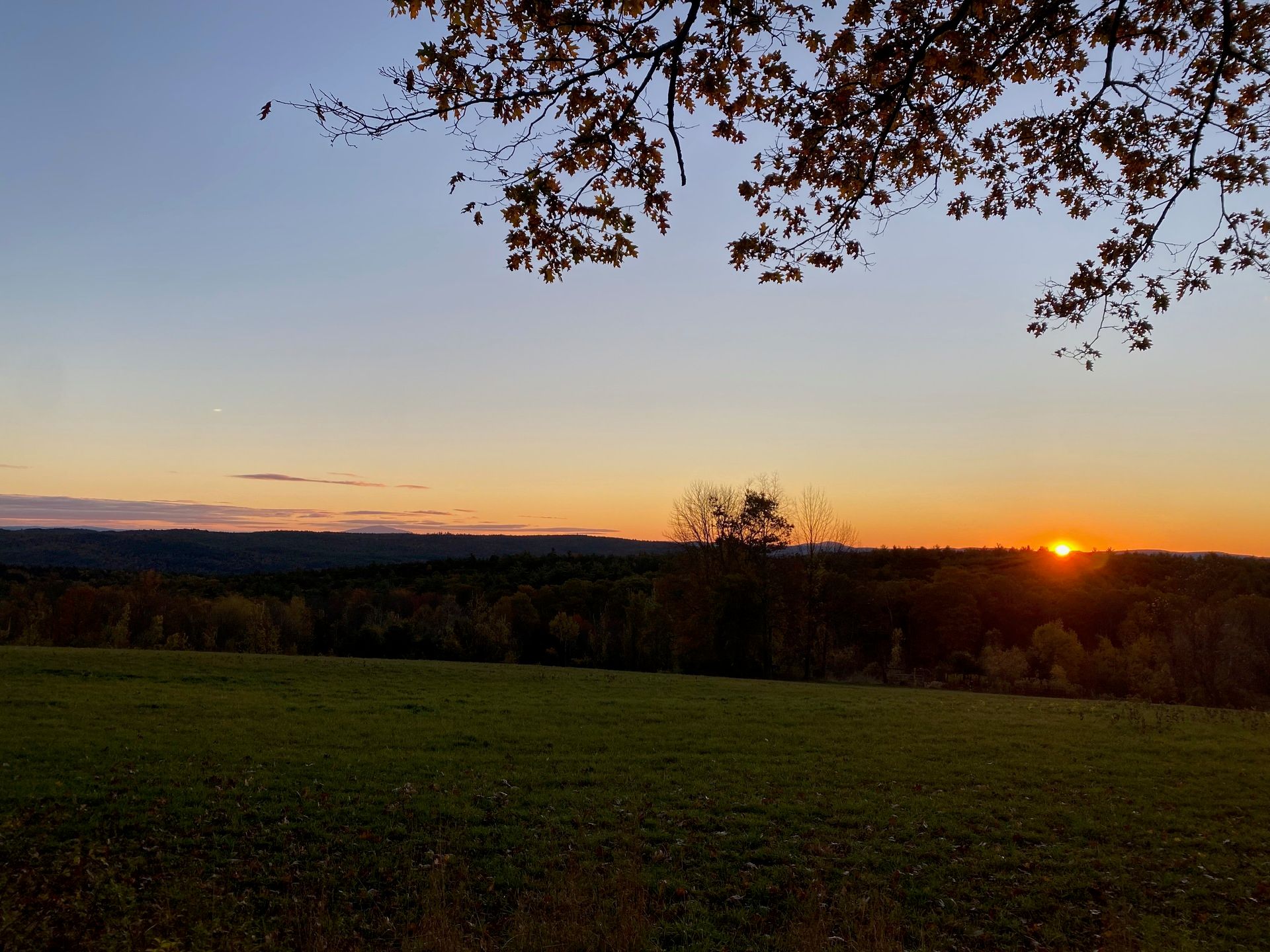 The sun rising behind the hills in front of a green pasture.