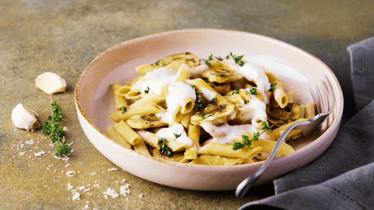 Creamy pasta dish with mushrooms and herbs served in a beige bowl, garnished with thyme and grated cheese.