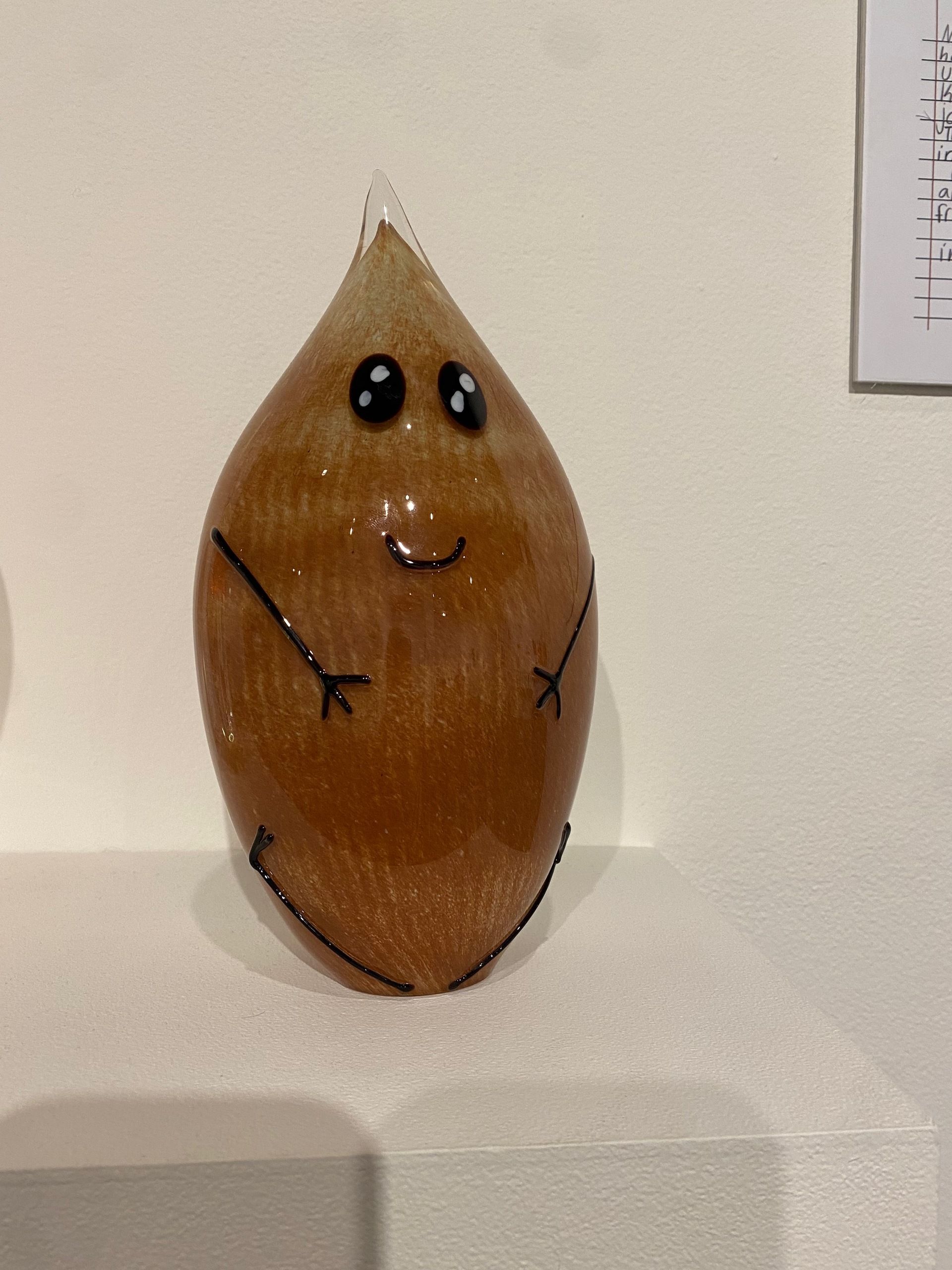 A small glass almond-creature, who is smiling, with small arms and legs.