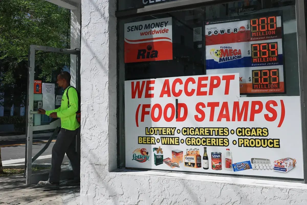 A person walks by a grocery store with a sign that says "WE ACCEPT (FOOD STAMPS)" 