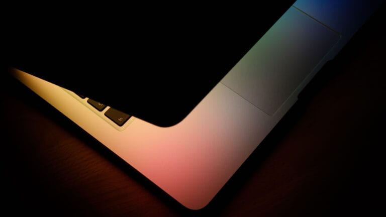Close-up of a partially closed laptop glowing with soft rainbow light, symbolizing technology and connection.