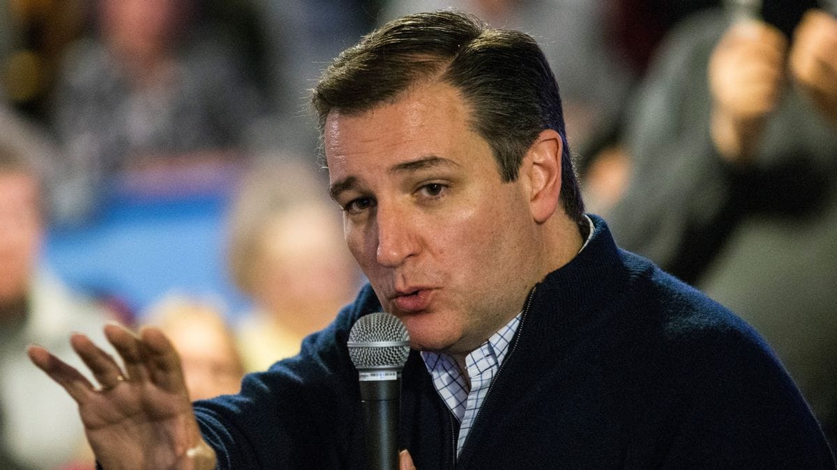A Latino looks with his left arm outstretched as he speaks into a microphone.