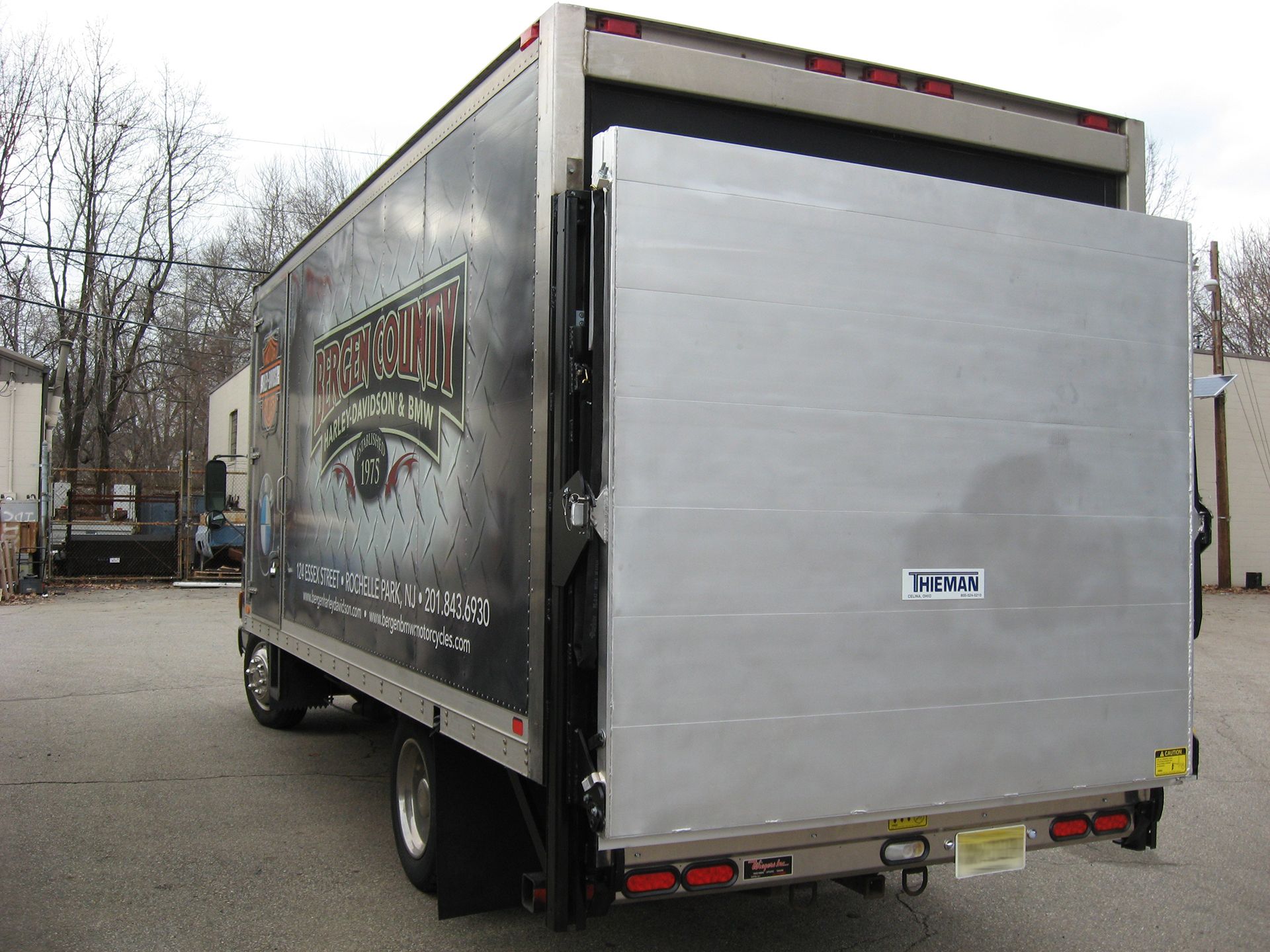 Thieman low-profile aluminum railgate fully closed on a box truck, showing large level-ride platform mounted to rear pillars for curbside loading.
