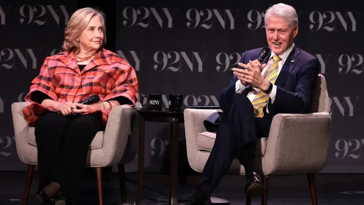 A white woman looks at a white man who's speaking to her right. Both are sitting down.