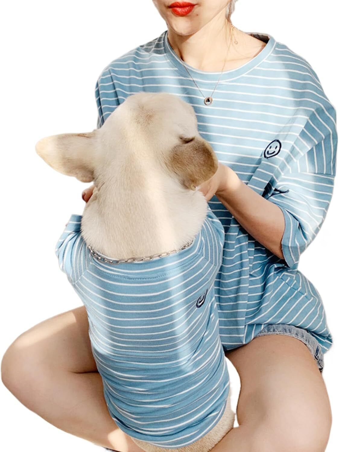 Matching Pet & Mom Pajamas A smiling woman and her dog wearing matching holiday pajamas with red plaid and snowflake designs, cuddled on the couch in a cozy living room.