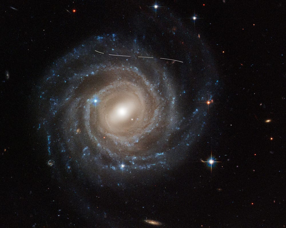 An image of a lovely face-on spiral galaxy with an arcing series of short lines moving across it.