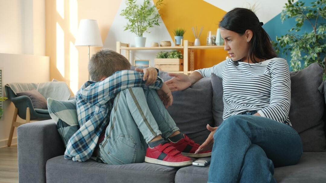 Strict woman is punishing little son wagging finger at child sitting on sofa crying feeling miserable. Punishment, naughty children and parenting issues concept.