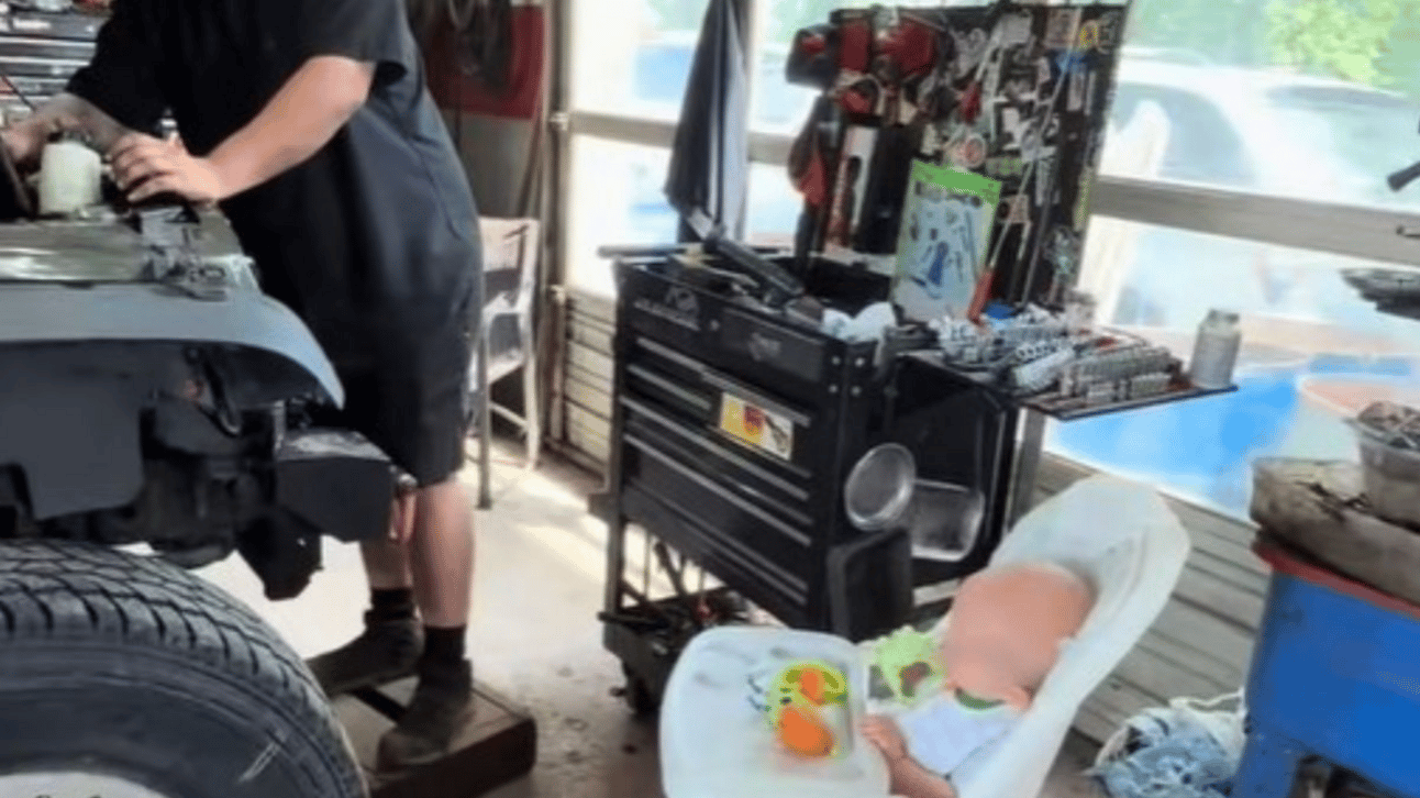 Image shows an infant in a highchair in a mechanic's garage. Shop sounds always soothe the crying baby.