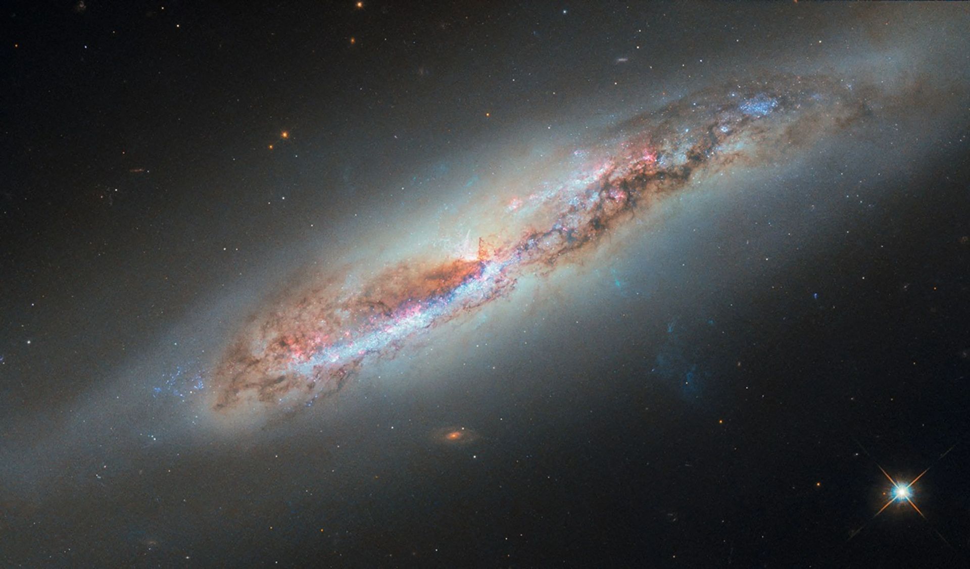 This Hubble image captures NGC 4388, a spiral galaxy about 60 million light‑years away in Virgo constellation. Seen nearly edge‑on, the galaxy reveals a plume of gas extending from its nucleus, an outflow not visible in Hubble’s 2016 observations. The feature likely formed as the galaxy moves through the Virgo Cluster’s hot intracluster medium, which strips gas from its disk and leaves it trailing behind. What makes the plume glow is less certain. Some of the ionization may come from the galaxy’s central supermassive black hole, whose accretion disk emits intense radiation, while shock waves farther out may energize more distant filaments. New multi‑wavelength data highlight this ionized gas, drawn from observing programs focused on galaxies with active black holes. 