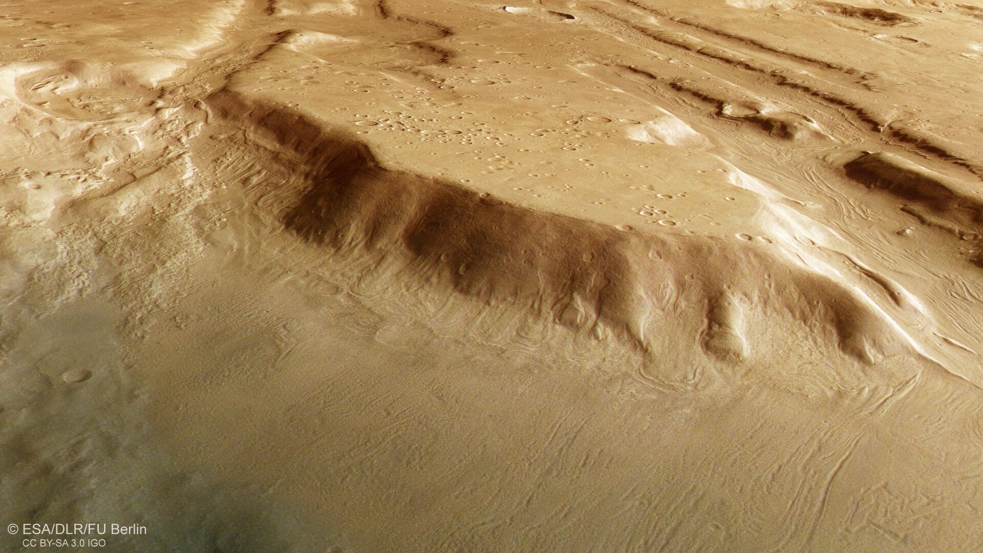 New imagery from ESA’s Mars Express reveals glacial remnants in Coloe Fossae, a mid-latitude region marked by deep valleys and craters. This image, created using data from ESA’s Mars Express High Resolution Stereo Camera, offers a top-down view of the Coloe Fossae region on Mars. The wavy surface patterns trace the paths of material movement during a past Martian ice age. The smoother, less cratered terrain near the base of the cliff suggests it formed more recently than the older, heavily cratered highlands above. The patterns, known as lineated valley fill and concentric crater fill, indicate slow-moving icy debris flows during the ice age. These features suggest that ice once extended far beyond the poles, likely driven by shifts in Mars’s axial tilt. The findings support broader evidence of cyclical climate change on Mars, with ice reaching as far south as 39°N as recently as 500,000 years ago.