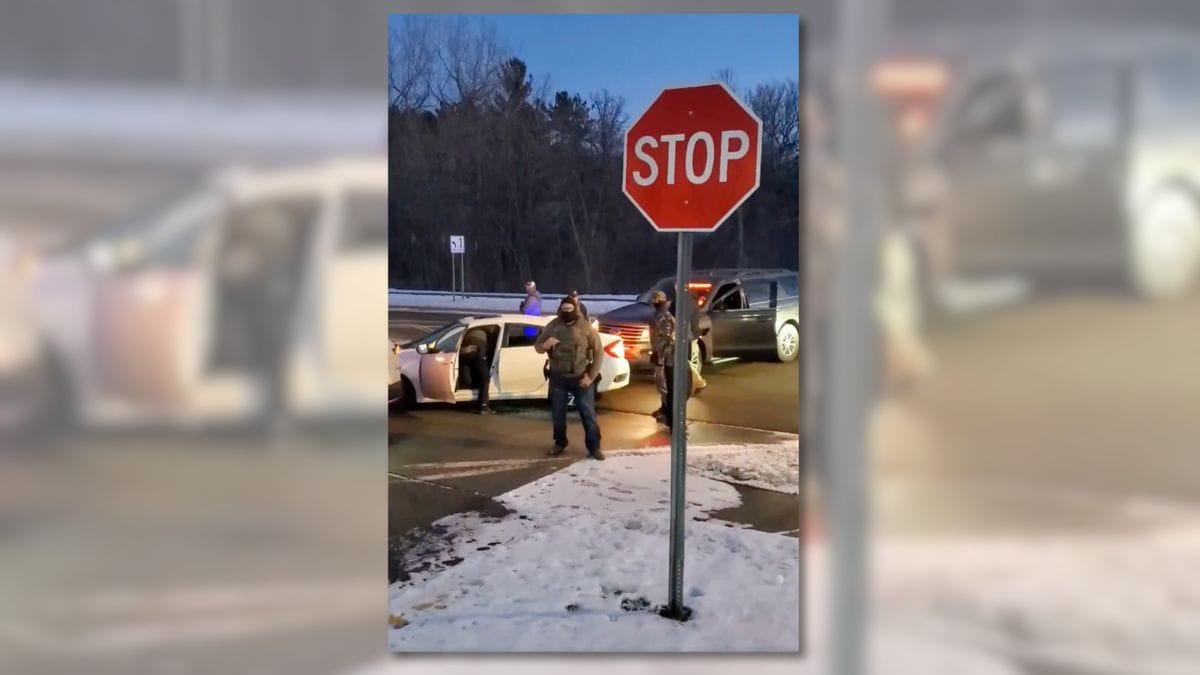 An image shows two cars involved in a crash on a road near a stop sign. People can be seen standing around the cars.