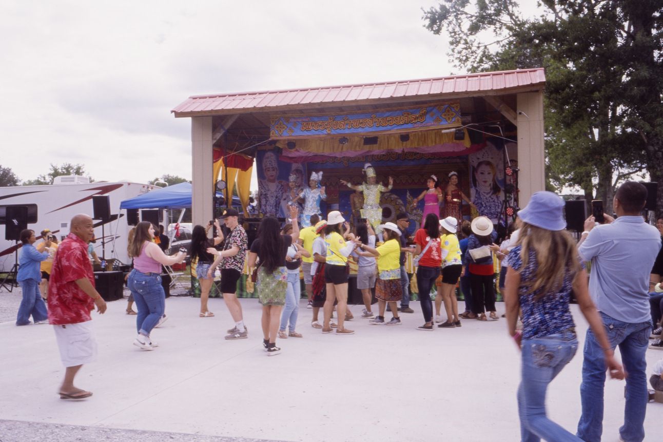 A multicultural crowd dances to Lao music in front of a stage with performers.