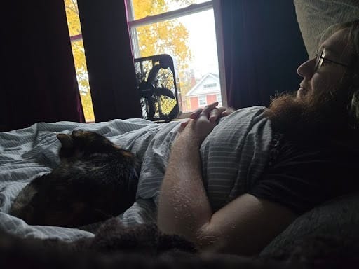 Picture of a calico cat curled up on the waist of a weird, bearded kid with glasses,