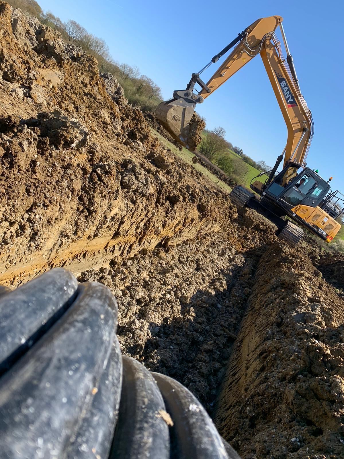 Sany excavator digging trenches for ground source heat pump collector loops with HDPE piping in the foreground
