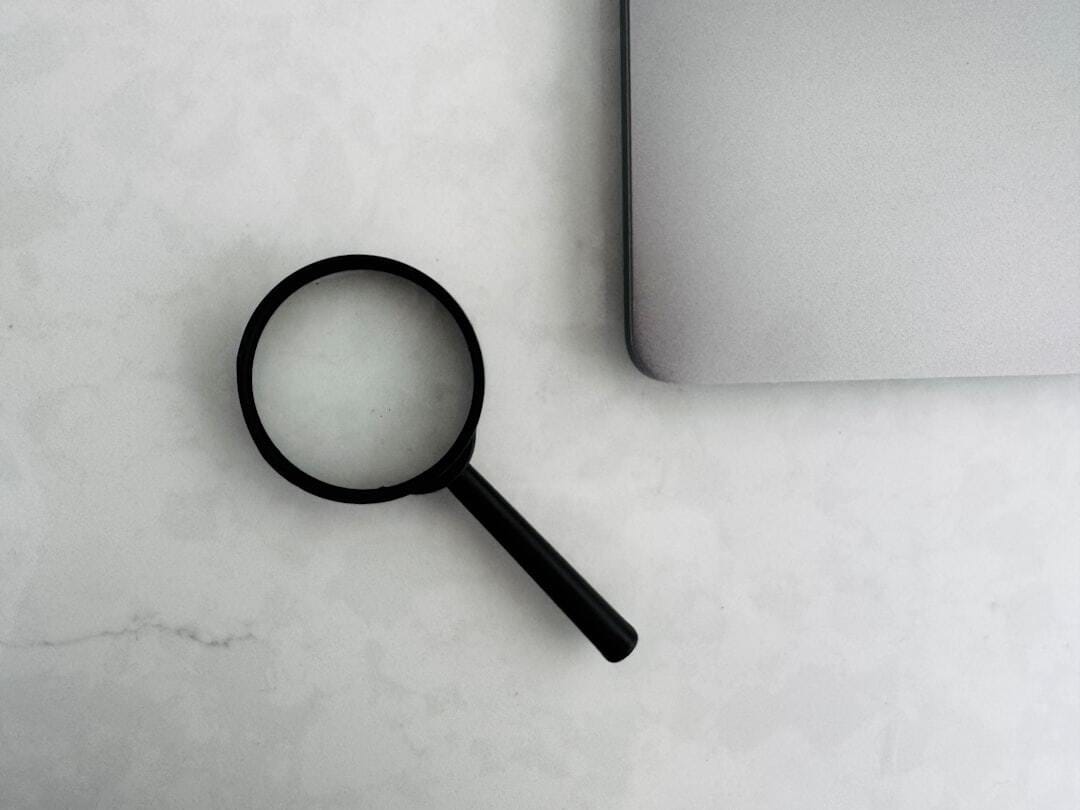 Magnifying glass beside the corner of a laptop on a marble surface