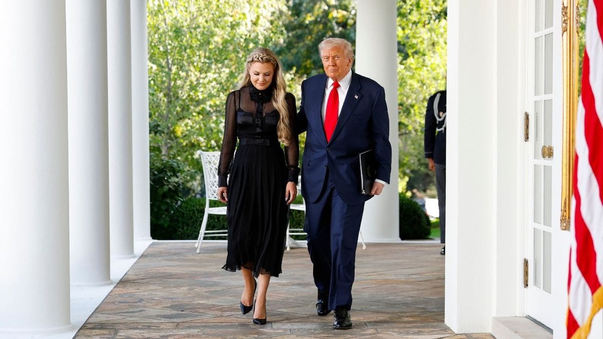 A white woman with blonde hair wearing a black dress and shoes walks next to a white man wearing a dark blue suit.