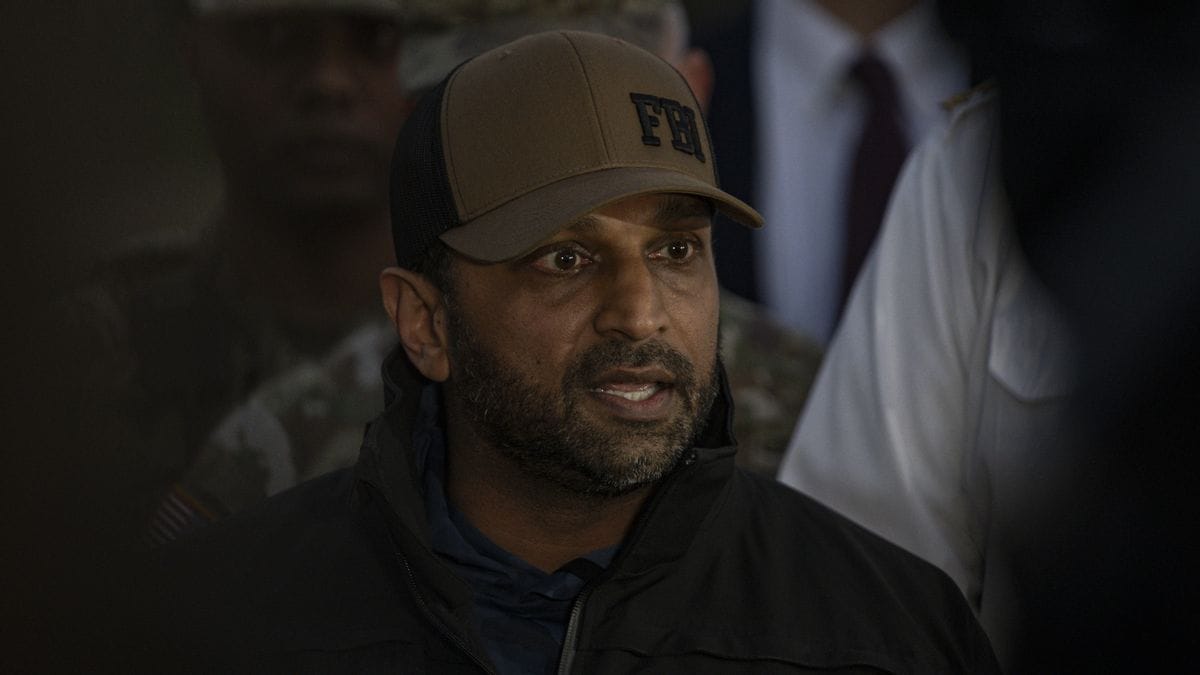 A South Asian man wearing a FBI hat appears to speak. You can faintly see people surrounding him.