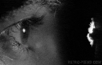 black and white close up of an eye looking through a hole in the wall