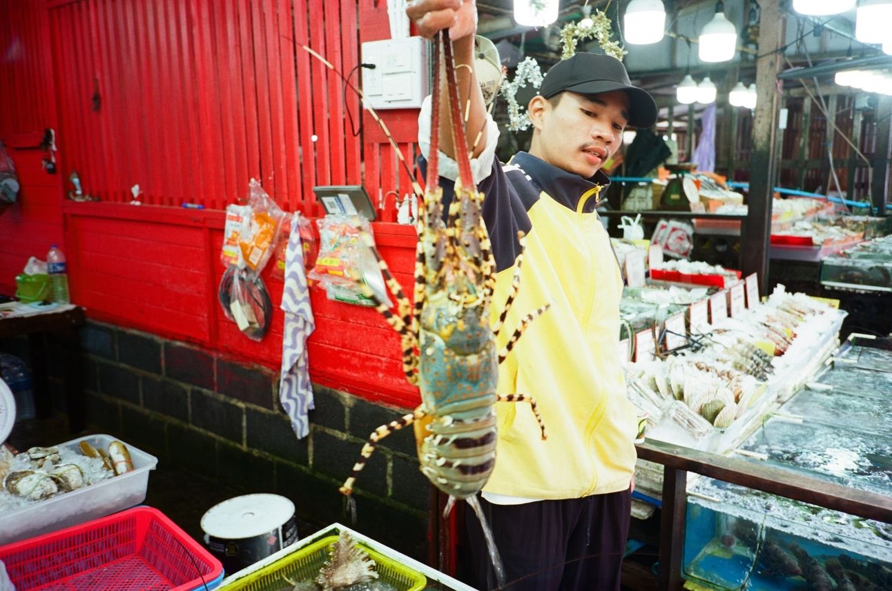 A fish monger holds up a lobster at an open air seafood market.