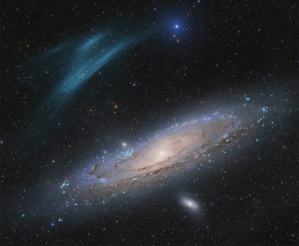 The Andromeda galaxy is a tilted spiral galaxy occupying most of the shot. To its upper left are a pair of arcing, delicate blue cirrus-like clouds.