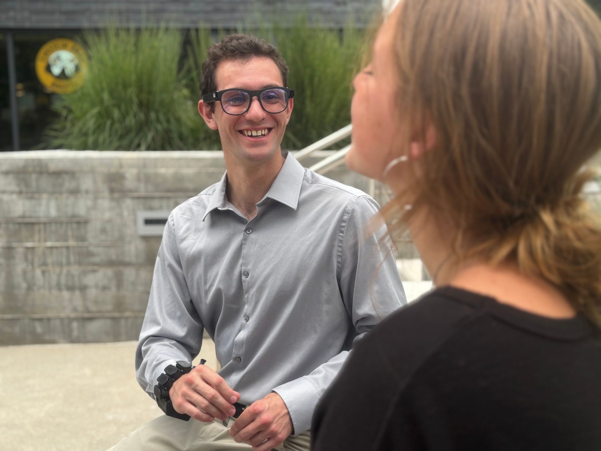 Person smiling while wearing AlEye glasses and wristband in a conversation.