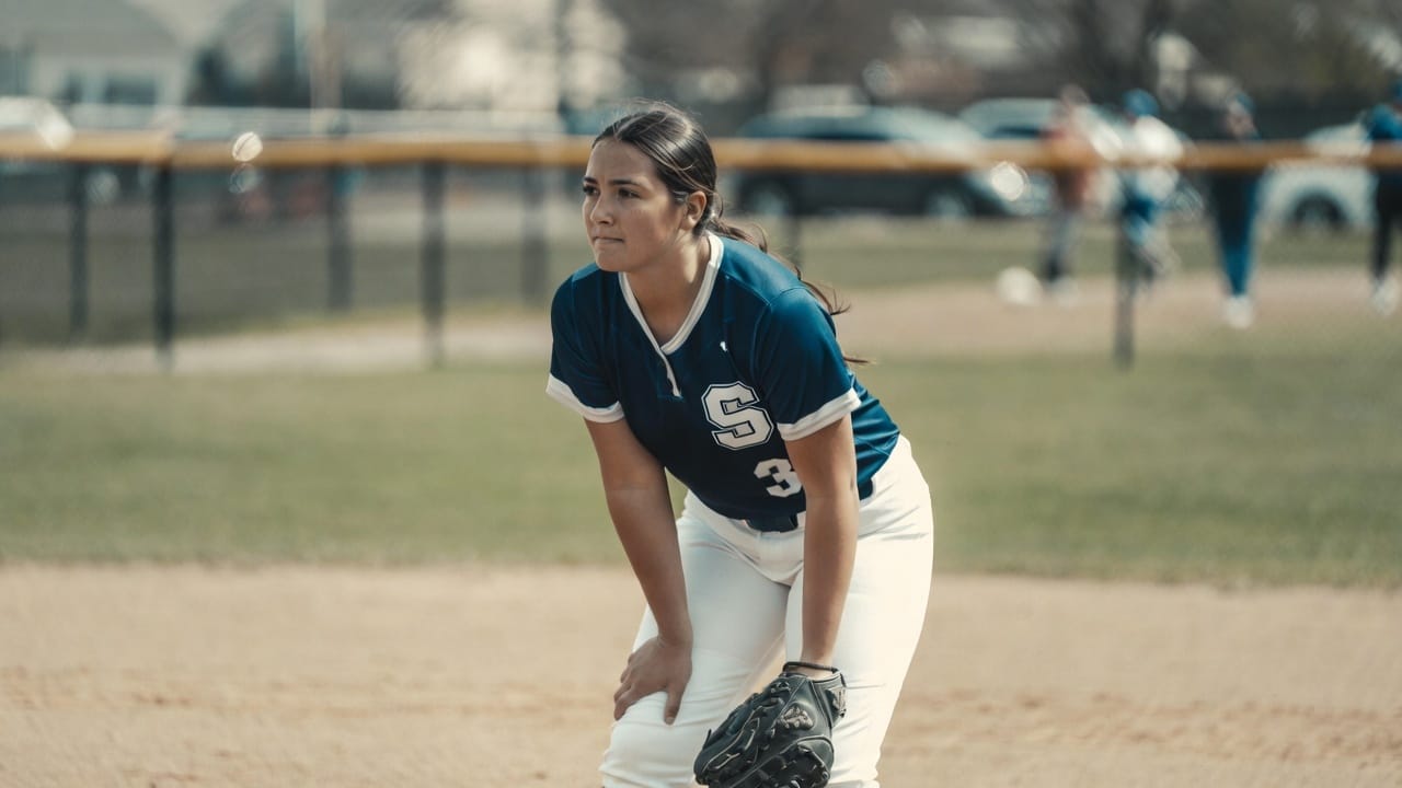 High school softball player in a ready position between plays, maintaining focus and composure during a game.