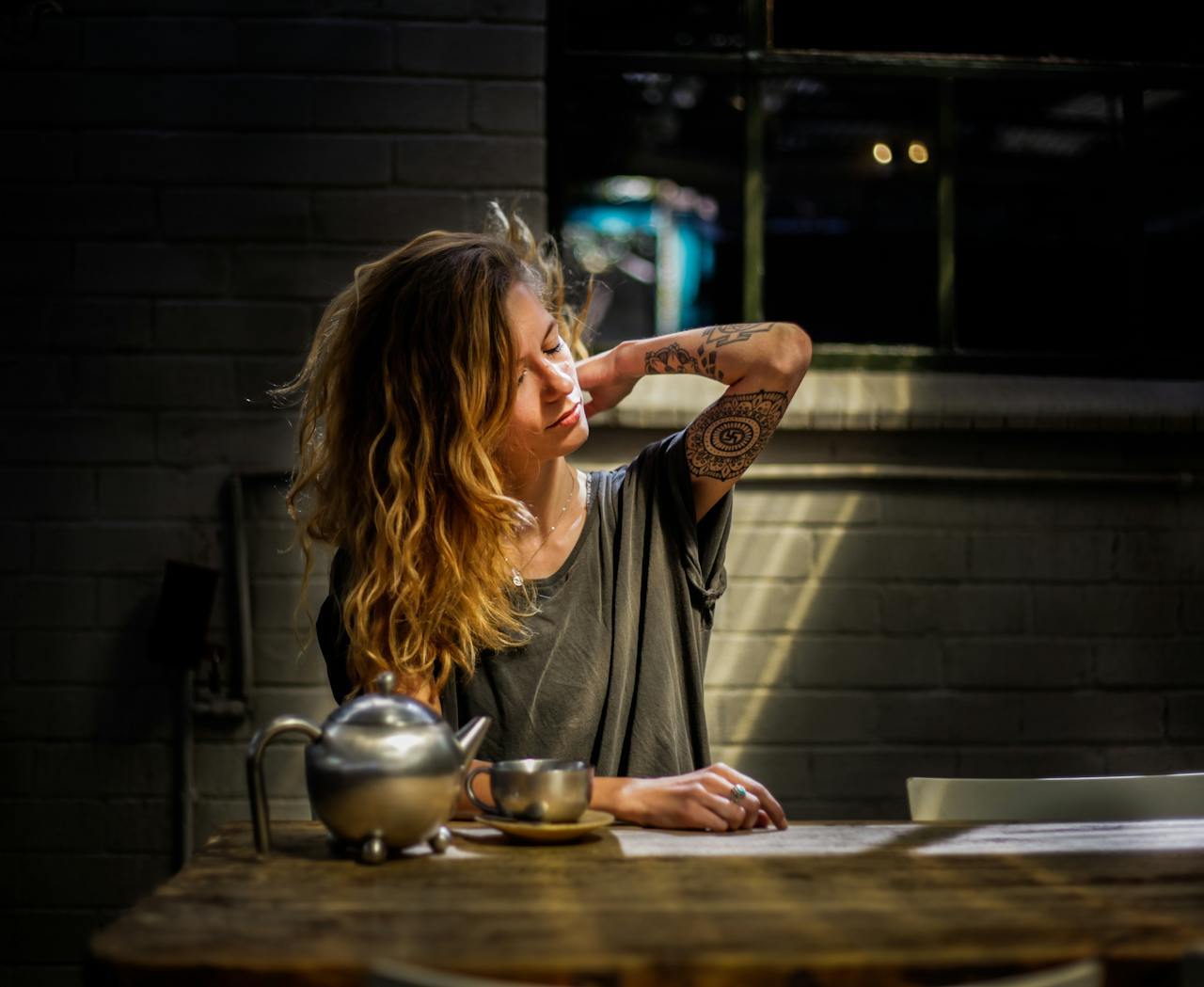 tired lookign woman sitting with a tea pot rubbing her neck