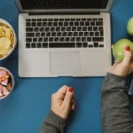 Work Space With Laptop, Candy, Chips, Water And Apple And Woman