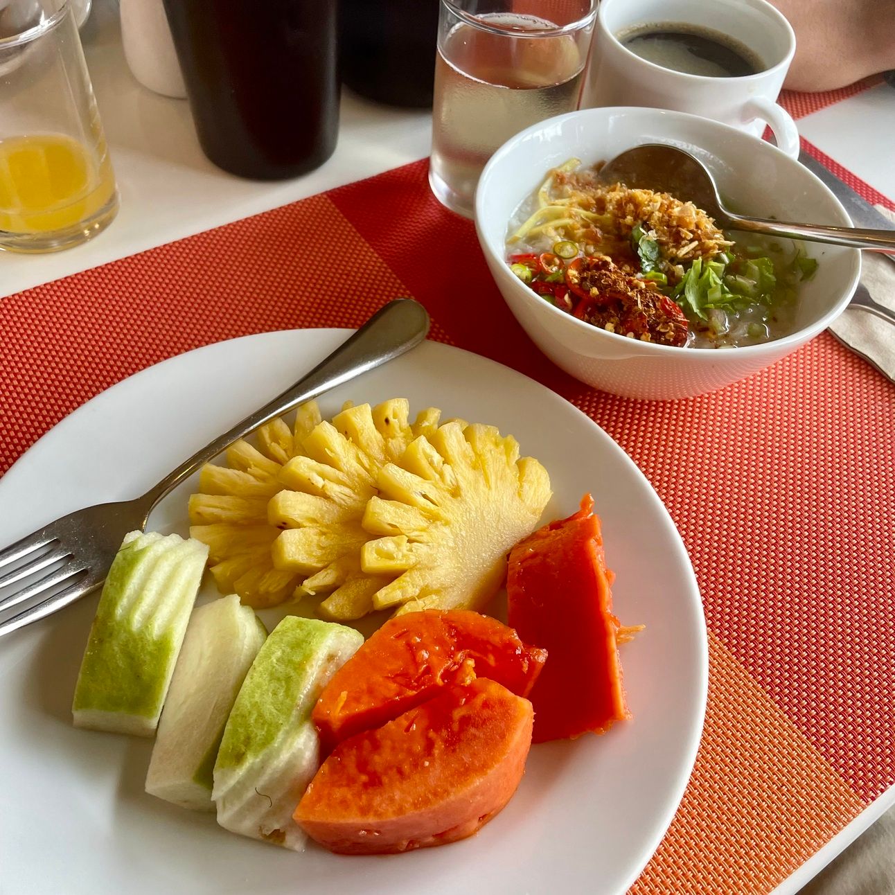 A breakfast of coffee, papaya, pinapple, guava, and rice soup.