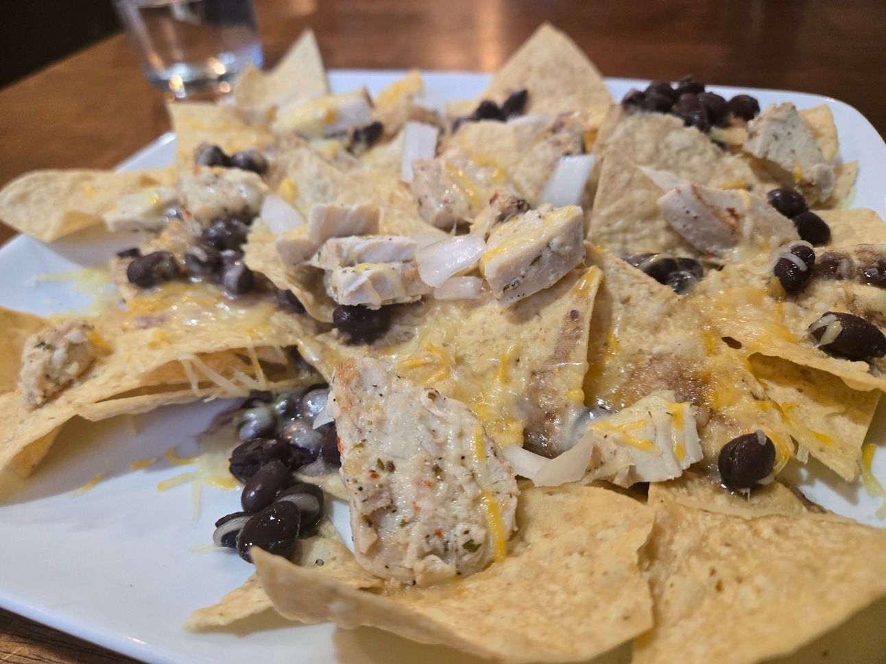 A plate of tortilla chips toped with melted shredded cheese, onions, grilled chicken, and black beans.