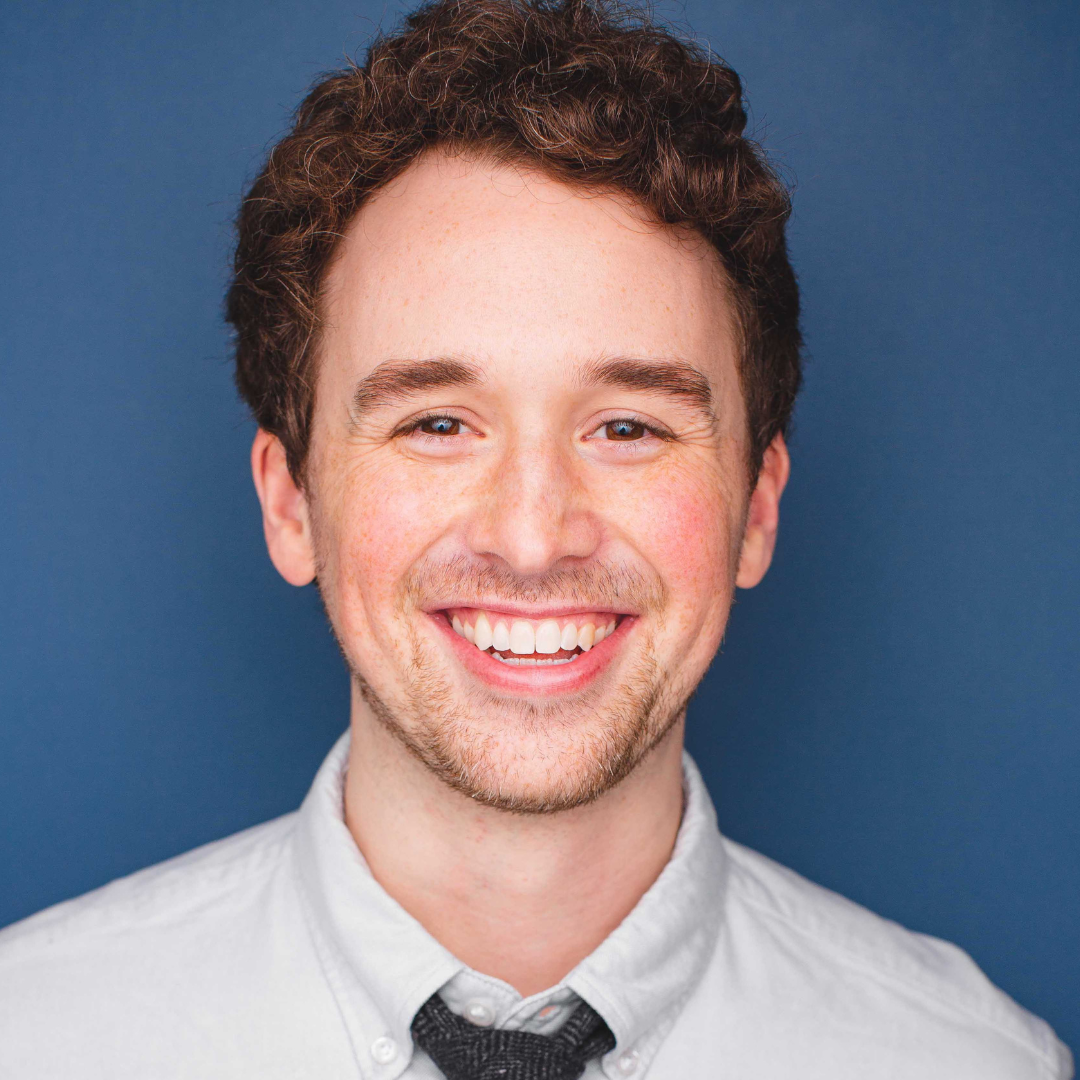 Patrick, contributing writer at AiNews.com, smiling in front of a solid blue background, wearing a white shirt and black tie.