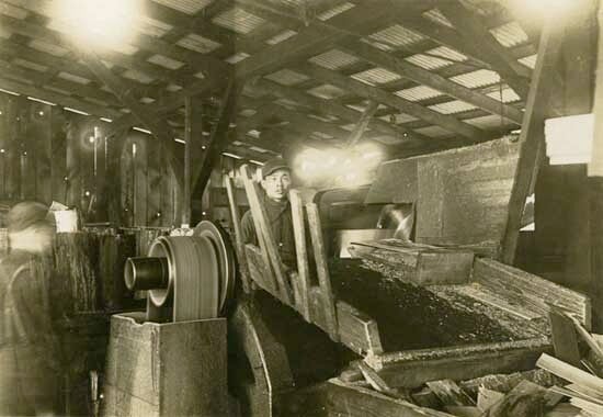 A Chinese worker stands behind a machine at a New Westminster sawmill around 1920. / New Westminster Museum and Archives IHP8537